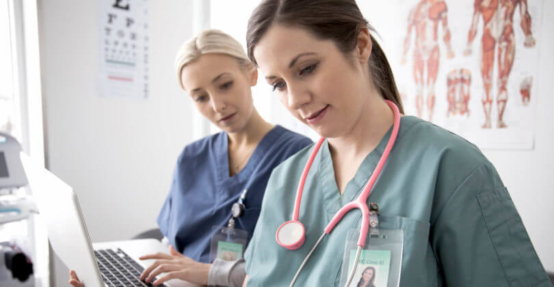 Picture of two nurses, representing the medical care available in San Jose, Costa Rica.  The picture shows the nurses in blue uniforms looking at a computer and holding some forms.